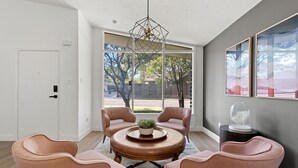 A modern living room with a round coffee table, four pink chairs, a hanging light fixture, and large windows offering a view of the outdoors. - 3 bdrm Sanctuary in the Heart of Dallas (Dallas)