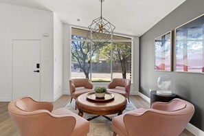 Relax in this serene living space with a view of the outdoors, featuring a large window, a round coffee table, and four comfortable armchairs.