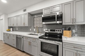 Modern kitchen with stainless steel appliances, white cabinetry, and a grey tiled backsplash.