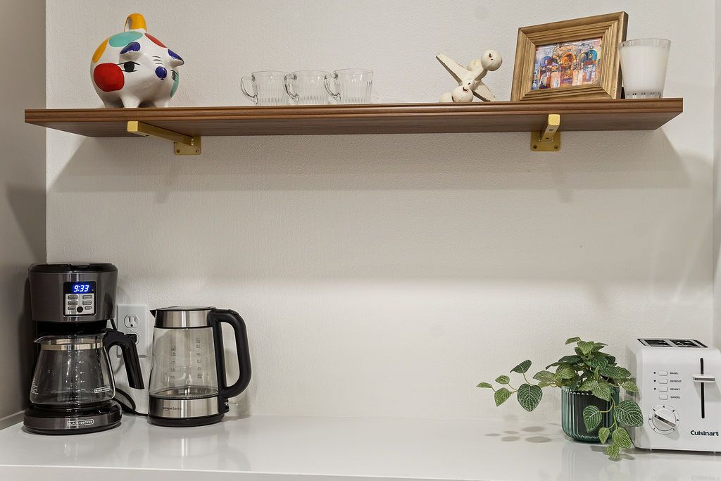 A kitchen counter with a coffee maker, a kettle, a toaster, and a shelf with decorative items.