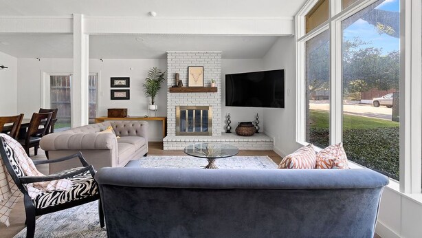 A modern living room with a white brick fireplace, a flat-screen TV mounted above it, and a large window offering a view of the outdoors. - 3 bdrm Sanctuary in the Heart of Dallas (Dallas)