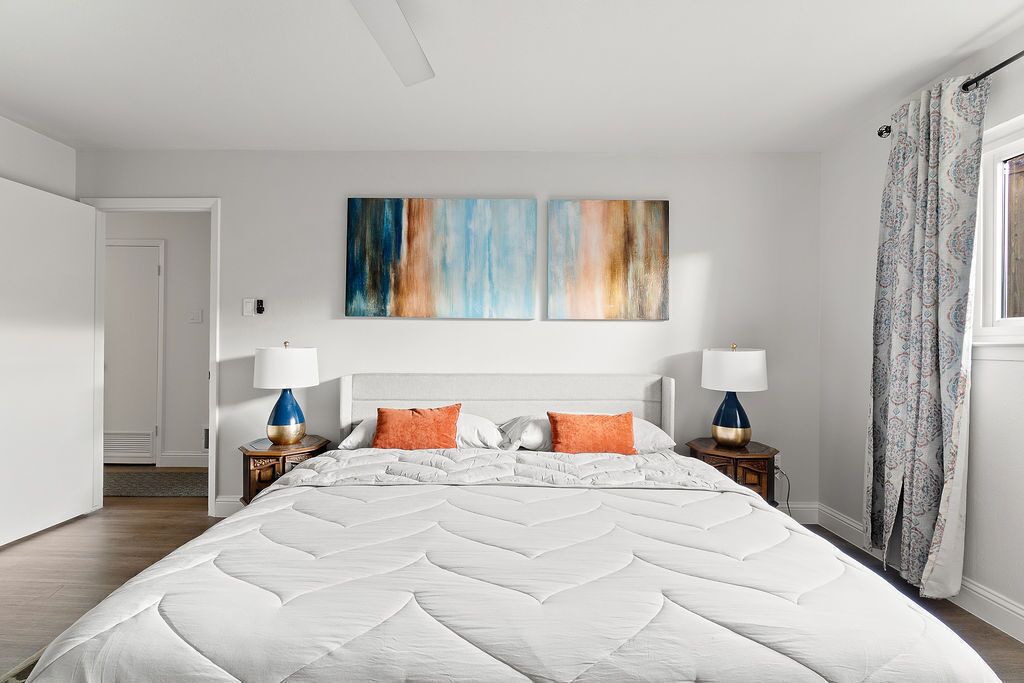 A bedroom with a large bed, two nightstands, a ceiling fan, and a window with curtains.