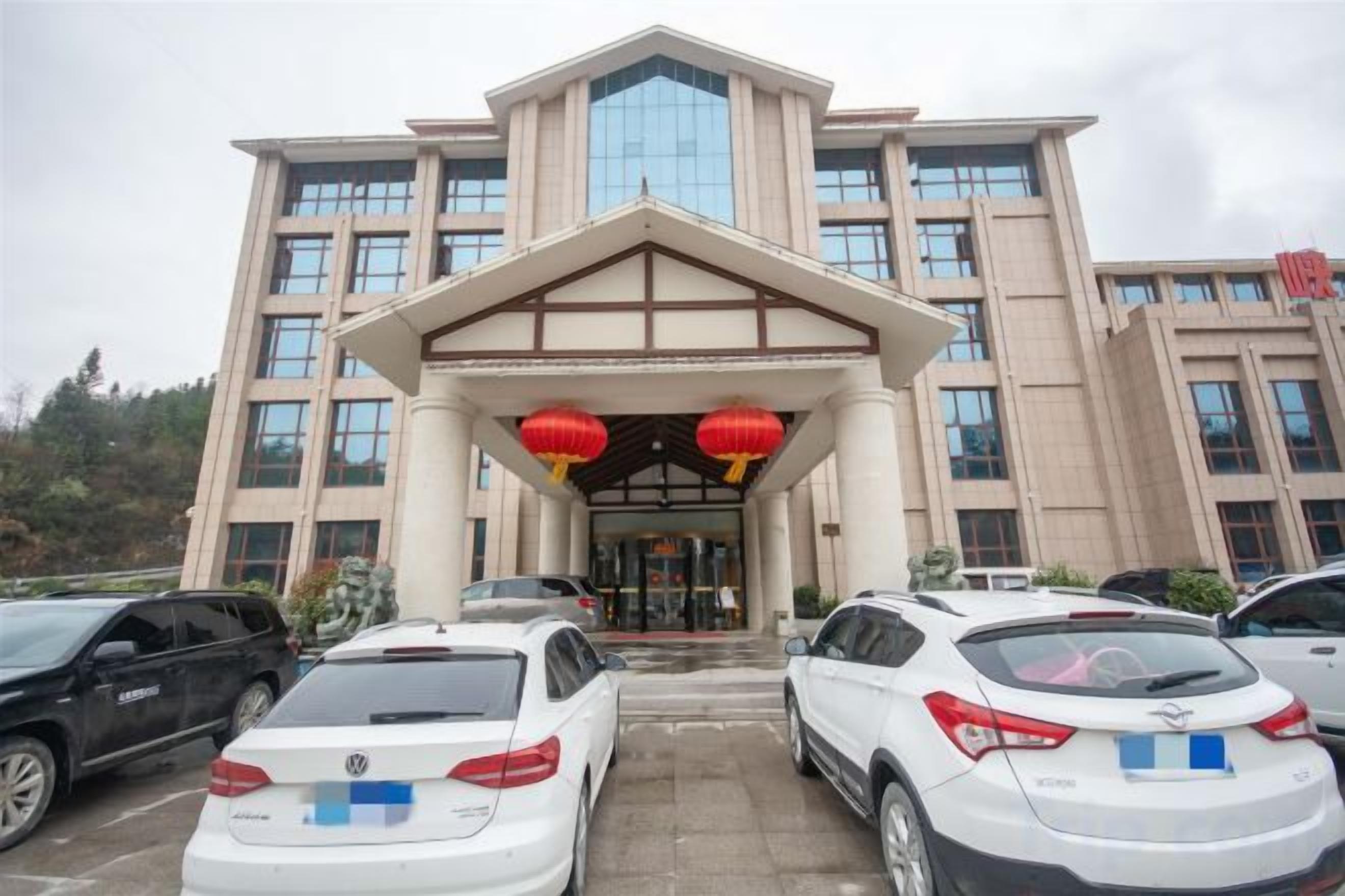 A multi-story building with a prominent entrance, several parked cars, and red lanterns above the entrance.