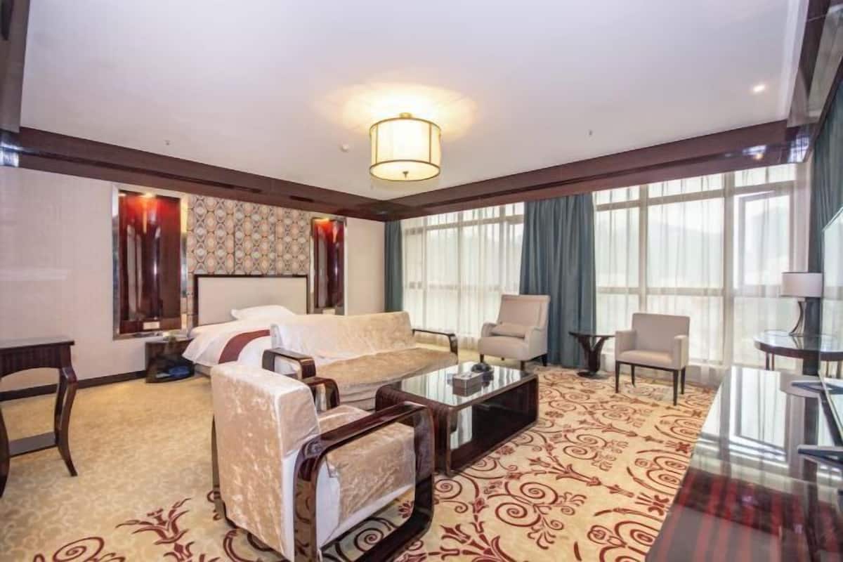 Habitació d'hotel amb un sofà, butaques, una taula de cafè, televisió i una finestra gran amb cortines.