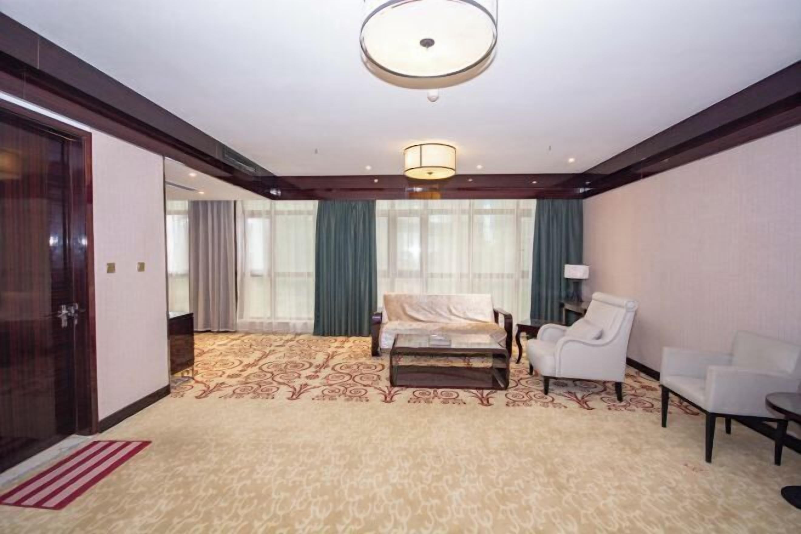 A hotel room with a bed, two chairs, a lamp, and a large window with curtains.