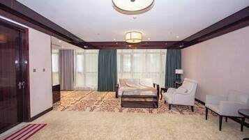 A hotel room with a bed, two chairs, a lamp, and a large window with curtains.