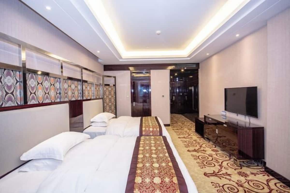 Habitació d'hotel amb dos llits, televisió i un passadís amb moqueta.