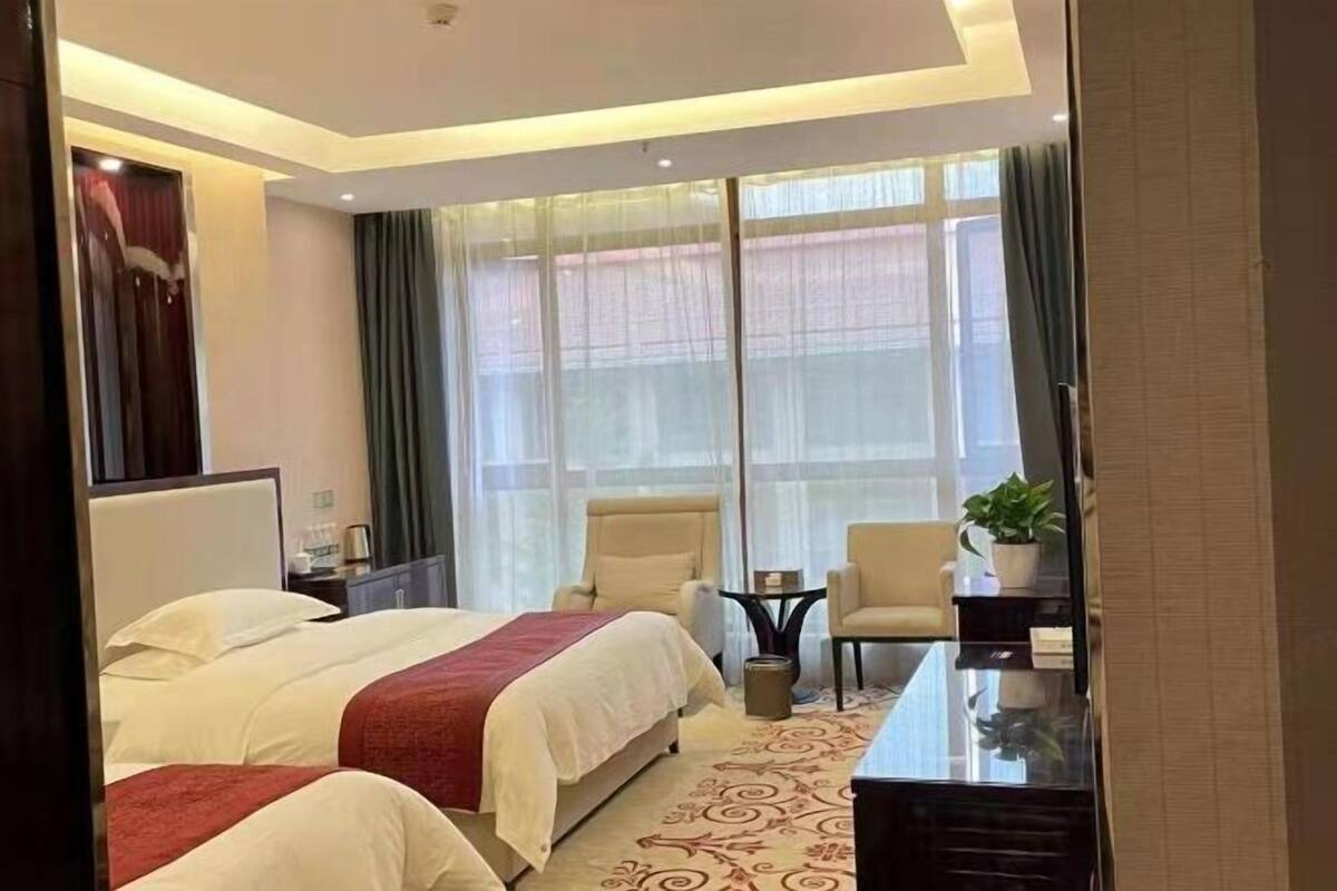 Habitació d'hotel amb dos llits, una taula de treball, una cadira, televisió i una finestra gran amb cortines.
