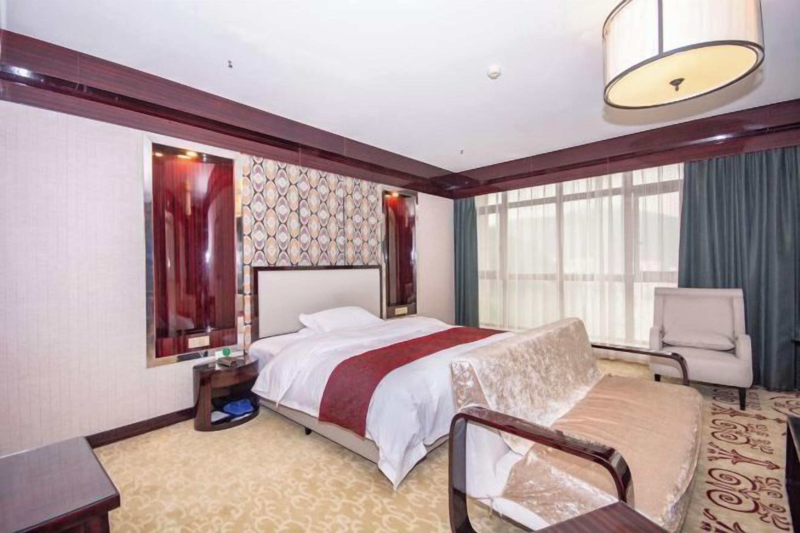 Habitación de hotel con cama, mesita de noche, silla y un ventanal con cortinas.