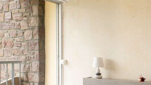 A bedroom with a stone wall, a wooden headboard, a white bed with pillows, a bedside lamp, and a radiator. - Sea-view apartment with two balconies in Erquy | 4 guests | Ref 442 (ERQUY)