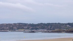 A coastal landscape with a sandy beach, calm water, and a hill with buildings in the background. - Sea-view apartment with two balconies in Erquy | 4 guests | Ref 442 (ERQUY)