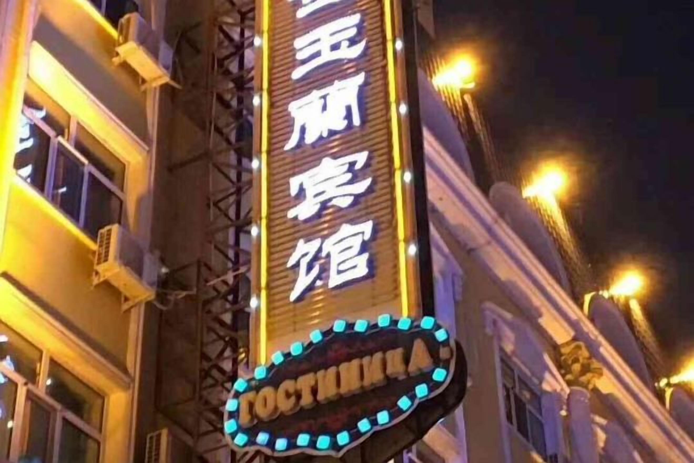 Un edificio con señalización iluminada, que incluye un letrero vertical destacado con texto y un letrero horizontal debajo.