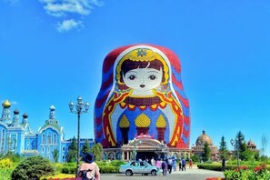 A large, colorful structure resembling a matryoshka doll in front of a building with domed architecture. - Jinyulan Hotel (Manzhouli)