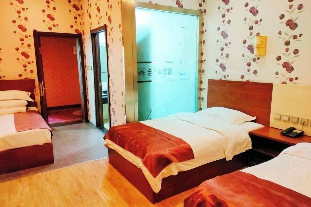 A hotel room with two beds, a wooden floor, a door, and a wall with a floral pattern.