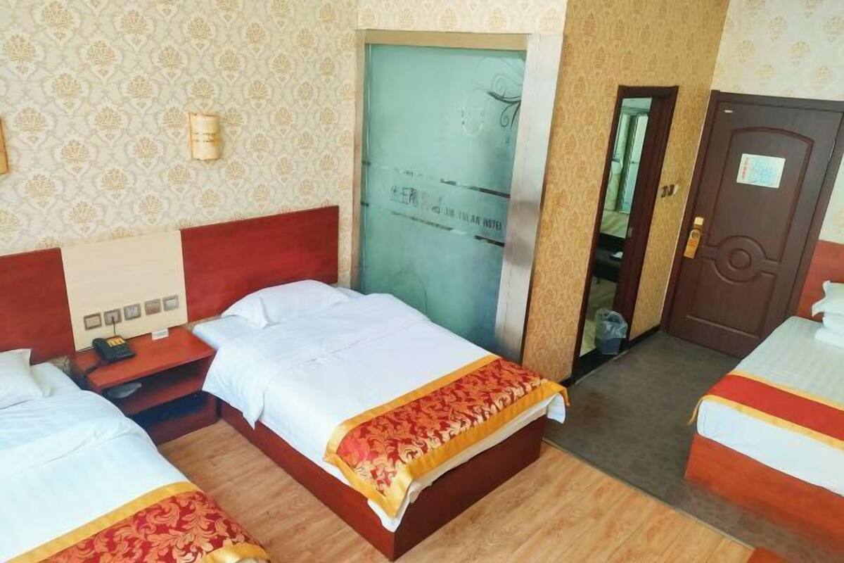 A hotel room with two beds, a wooden floor, a door with a sign, and a patterned wall.