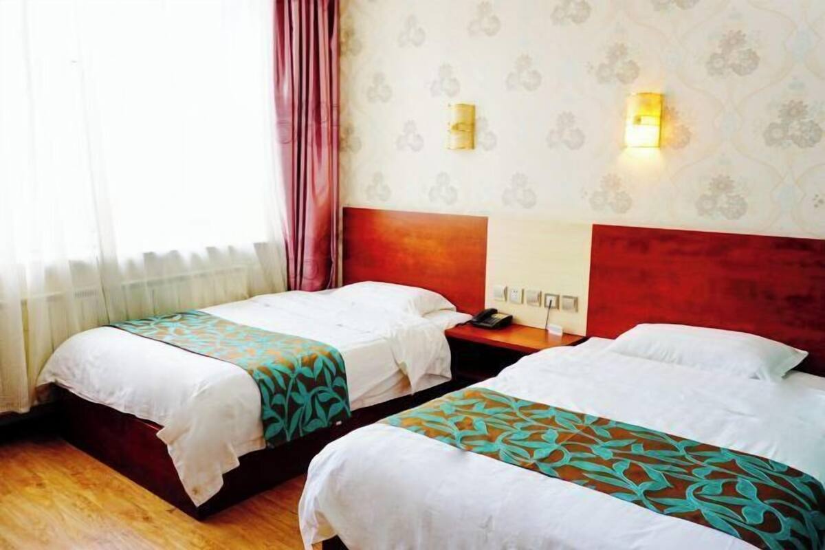 A hotel room with two beds, a wooden floor, a red headboard, and patterned wallpaper.