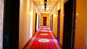 Pasillo de hotel con alfombra roja, puertas a ambos lados y techo con iluminación empotrada.