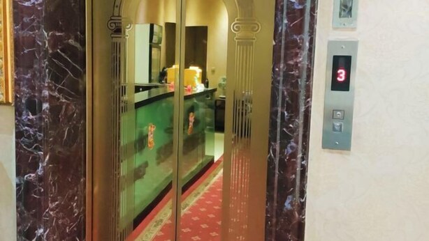 Un ascensor con una pantalla digital que muestra el número 3, un mostrador de recepción con alfombra roja y paredes de mármol.