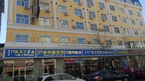 Un edificio de varios pisos con fachada amarilla y numerosas ventanas. Varias tiendas en la planta baja con rótulos en un idioma extranjero.