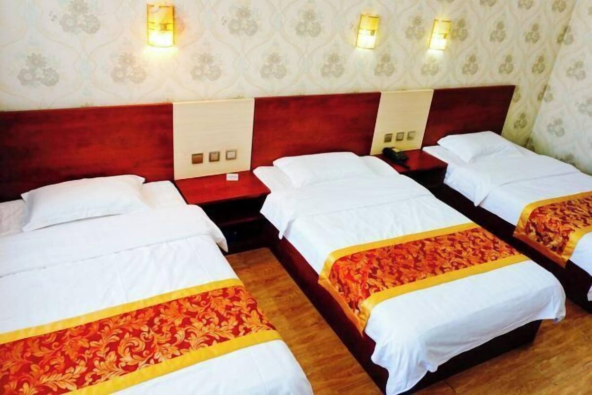 A hotel room with three beds, each with white linens and a red and yellow bedspread. There are wall-mounted light fixtures and a patterned wallpaper.
