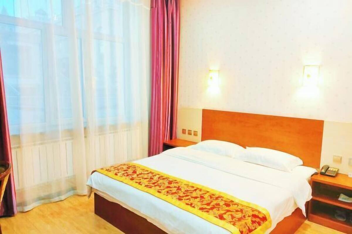 A hotel room with a bed, a nightstand, a telephone, and a window with curtains.