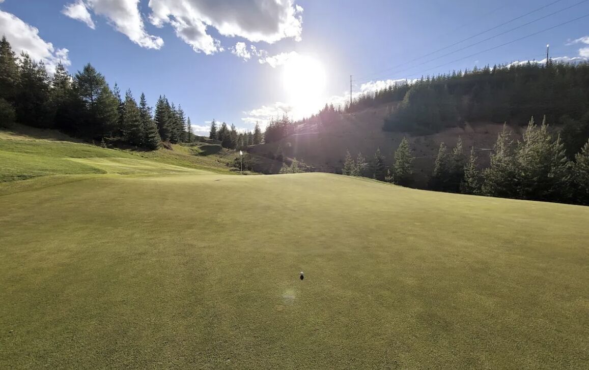 Un campo da golf con cielo sereno, alberi e un paesaggio luminoso.