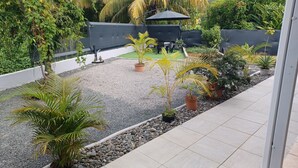 A patio area with a gravel ground, potted plants, a black umbrella, and a seating area with chairs and a table. - HONEY HOUSE VILLA WITH PRIVATE RIVER (Petit-Bourg)