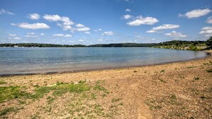 Ein Strand am Seeufer, mit blauem Himmel und Bäumen in der Ferne.