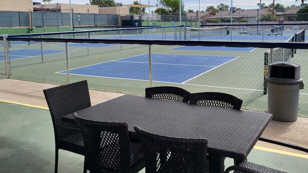 Ein überdachter Tennisplatz mit Sitzgelegenheiten und einem Mülleimer.