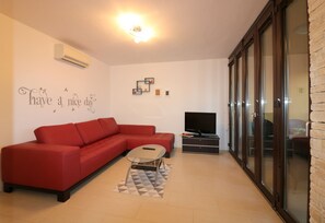 A living room with a red sofa, a small coffee table, a flat-screen TV, and a wall with a positive message.