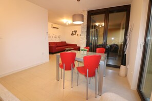 A modern living room with a red sofa, a dining table with four red chairs, and a glass door leading to a balcony.