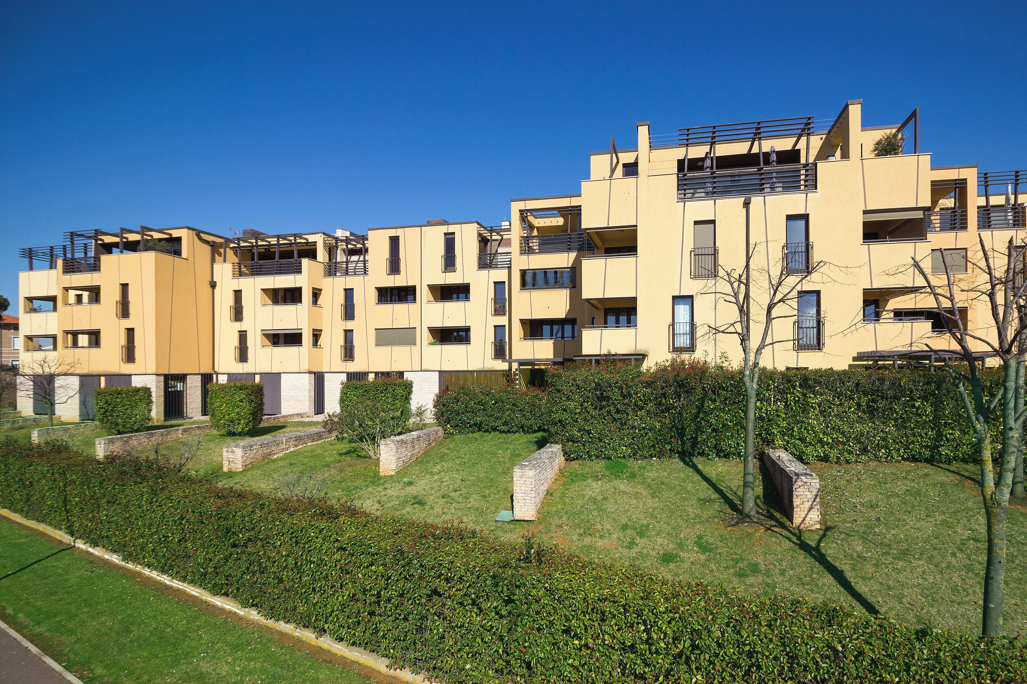 Un immeuble d’appartements moderne doté de nombreux balcons, d’une pelouse bien entretenue et surplombant un ciel d’un bleu éclatant.