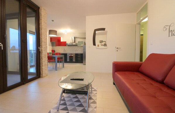 A modern living room with a glass coffee table, a red sofa, and a kitchen in the background.