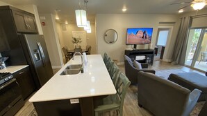 A modern kitchen with a central island, a dining area with chairs, a sofa, and a television in the living room.