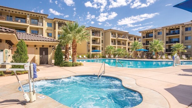 A hotel with a swimming pool, palm trees, and a clear blue sky.