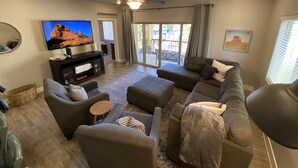 A living room with a large flat-screen TV, a ceiling fan, and a sliding glass door leading to an outdoor patio.