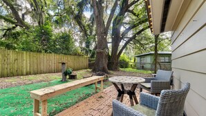 A backyard with a wooden deck, a round table, wicker chairs, a bench, and a small shed.