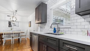 A modern kitchen with white countertops, dark cabinetry, and a window with blinds.