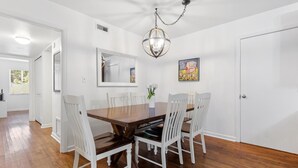 A dining room with a wooden table and white chairs, a chandelier, and a mirror on the wall.