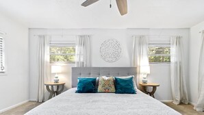 A bedroom with a large bed, two bedside tables with lamps, a ceiling fan, and a decorative wall piece.