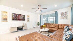 Un salon spacieux avec un canapé en cuir marron, un meuble de rangement blanc pour les appareils électroniques et un grand tableau accroché au mur.