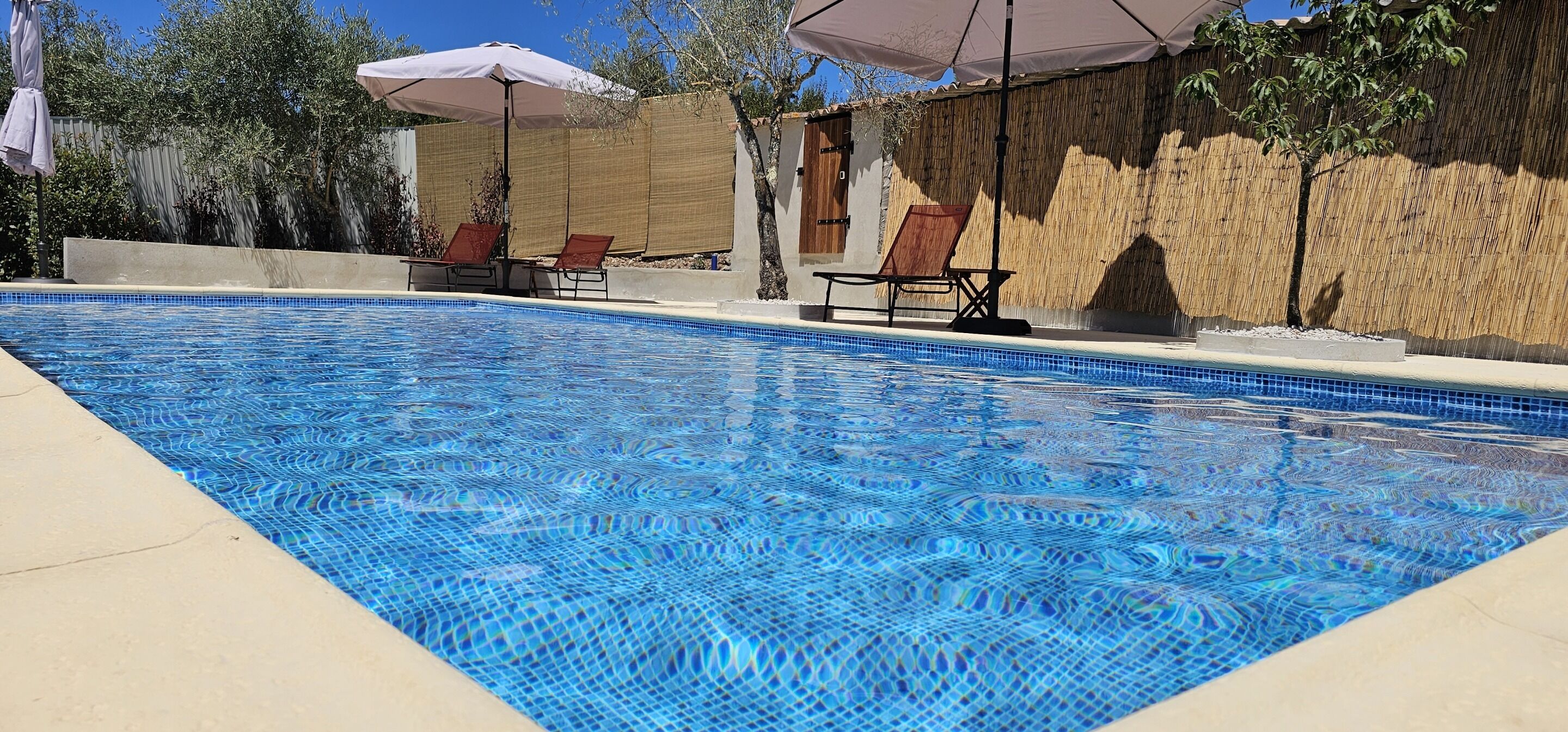 Una piscina con agua azul cristalina, rodeada de sillas de descanso y sombrillas.