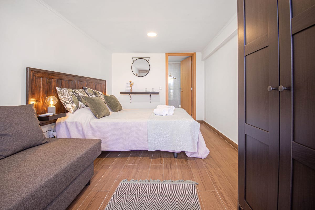 A bedroom with a bed, a nightstand, a bedside table, a dresser, a mirror, and a door.