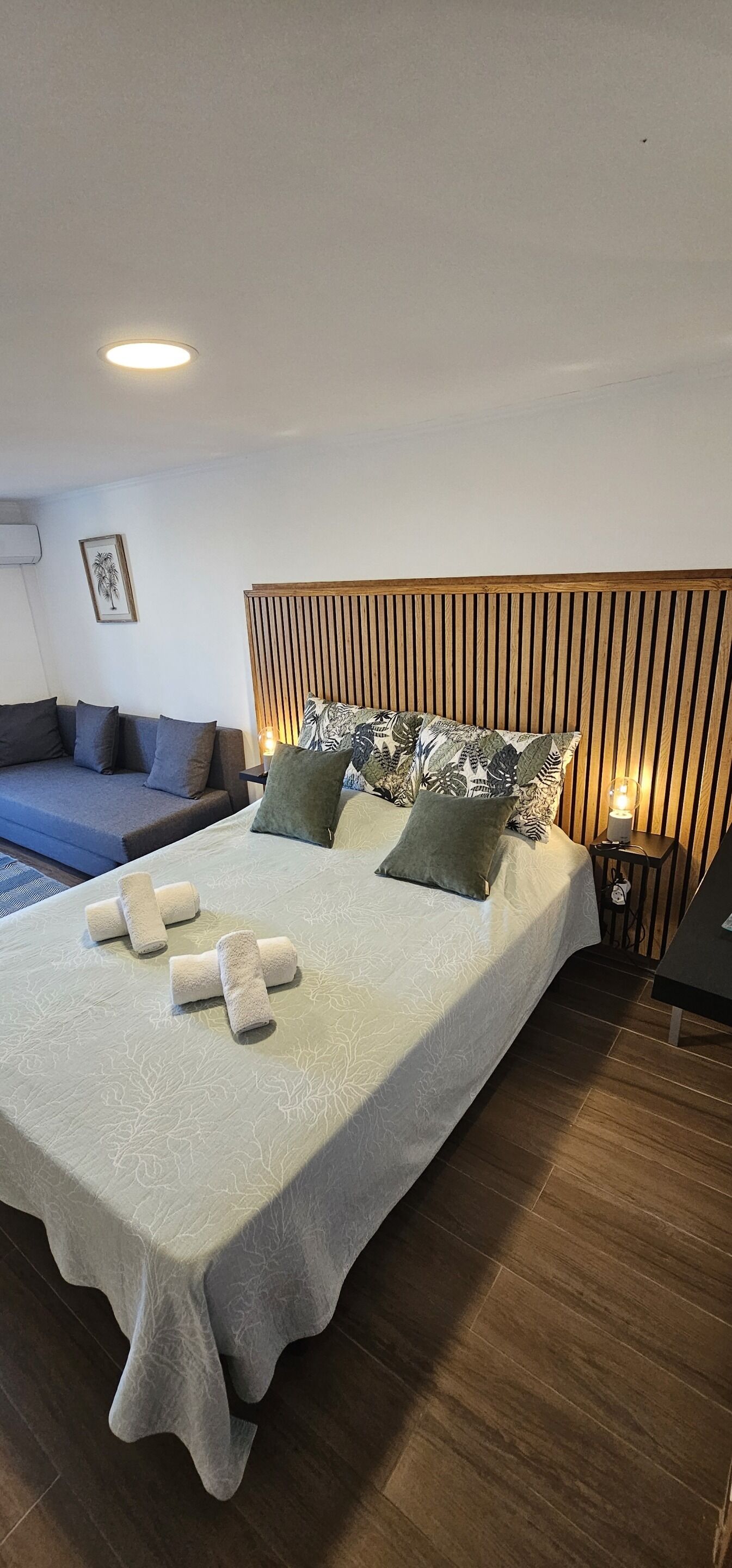 A modern bedroom with a large bed, a wooden headboard, and a blue sofa.