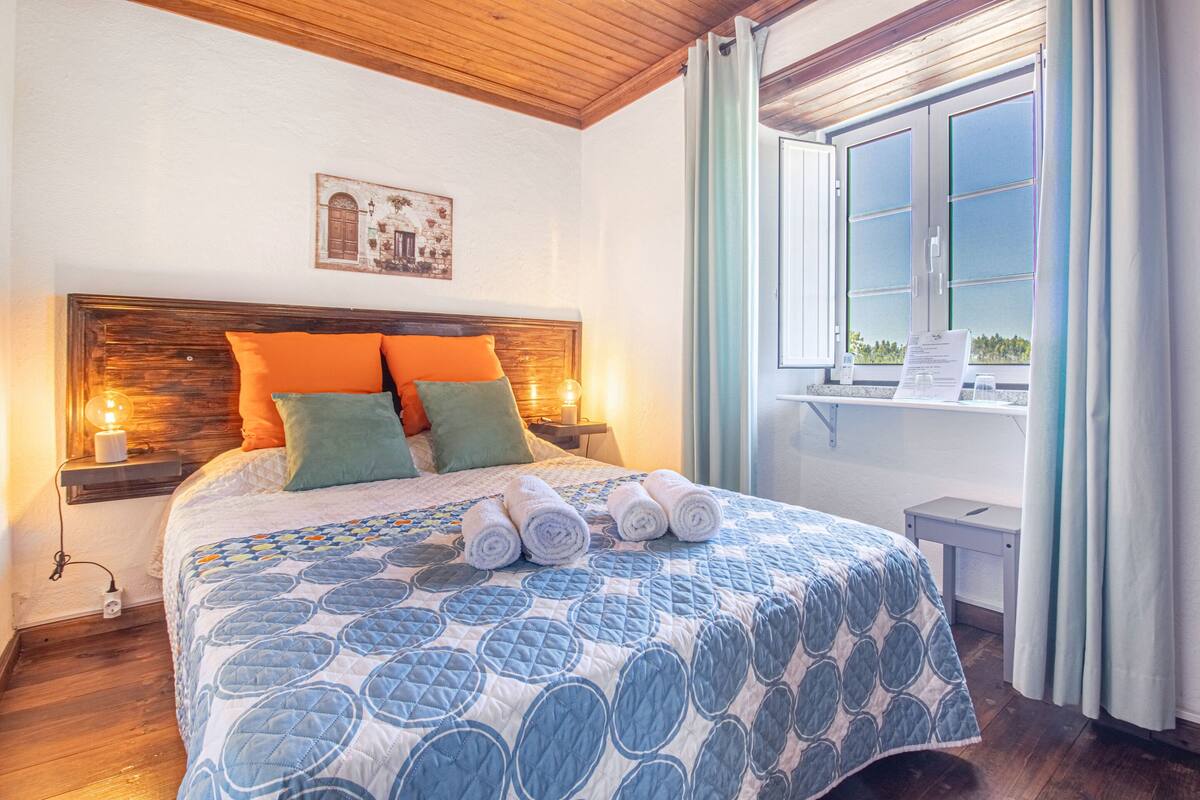 A bedroom with a wooden headboard, a quilted bedspread, and a window with curtains.