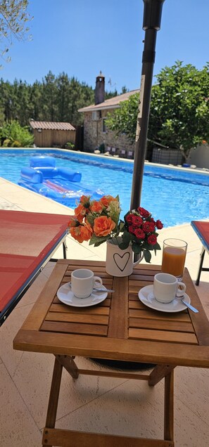 A wooden table with two white cups and saucers, a vase with orange and red flowers, and a glass of orange juice by a pool. - Quinta Penedo das Antas (Serta)