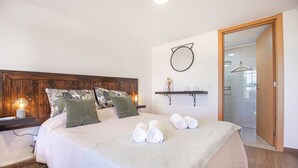 A neatly made bed with pillows and rolled towels, a bedside table with a lamp, and a wooden headboard. - Quinta Penedo das Antas (Serta)