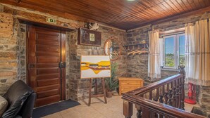 A rustic room with a wooden door, a painting on easels, a mirror, and a view through a window with curtains. - Quinta Penedo das Antas (Serta)