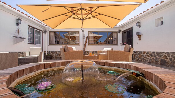 A patio area with a fountain, wicker furniture, and a large umbrella. - Quinta Penedo das Antas (Serta)