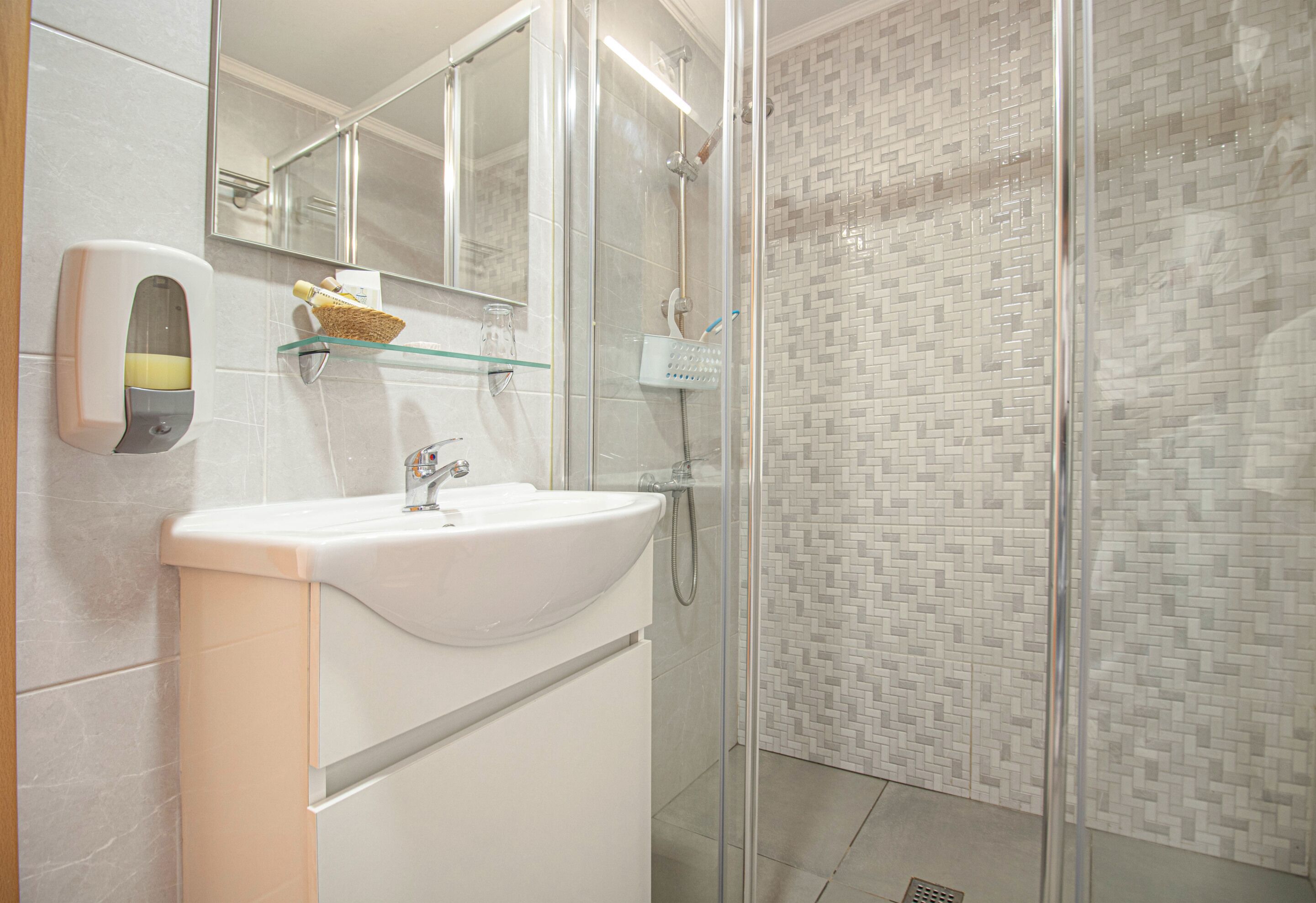 Un baño moderno con un lavabo blanco, cabina de ducha con mampara de vidrio y pared de ducha con azulejos.